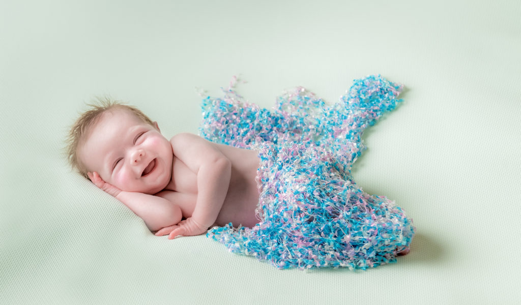 laughing baby wrapped in a knitted blanket during a newborn baby photoshoot in West Yorkshire