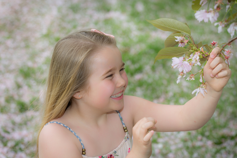 A smiling girl pulls blossom from a tree