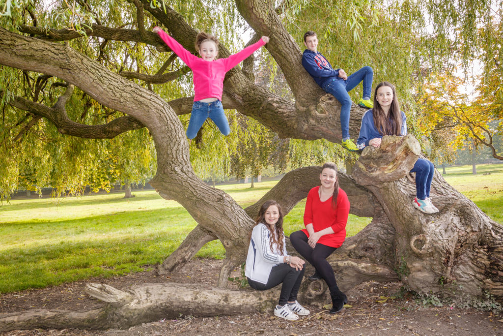 A family pose on a large fallen tree in Horbury village. Carr Lodge Park, West Yorkshire. Family photo shoot.