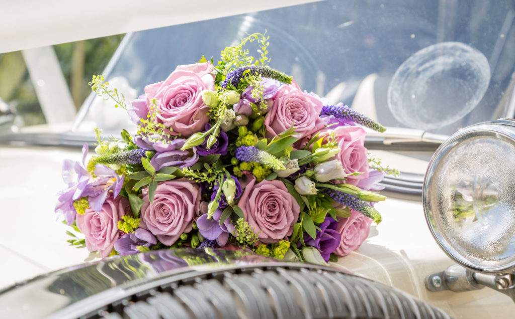 A bouquet of flowers in pink and purple flowers on the bonnet of a wedding car